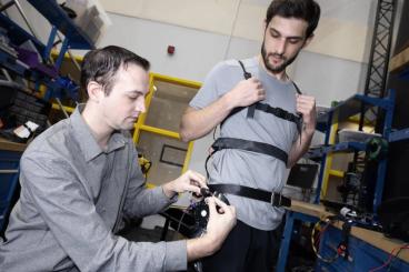 Researcher Aaron Young makes adjustments to an experimental exoskeleton worn by then-Ph.D. student Dean Molinaro.